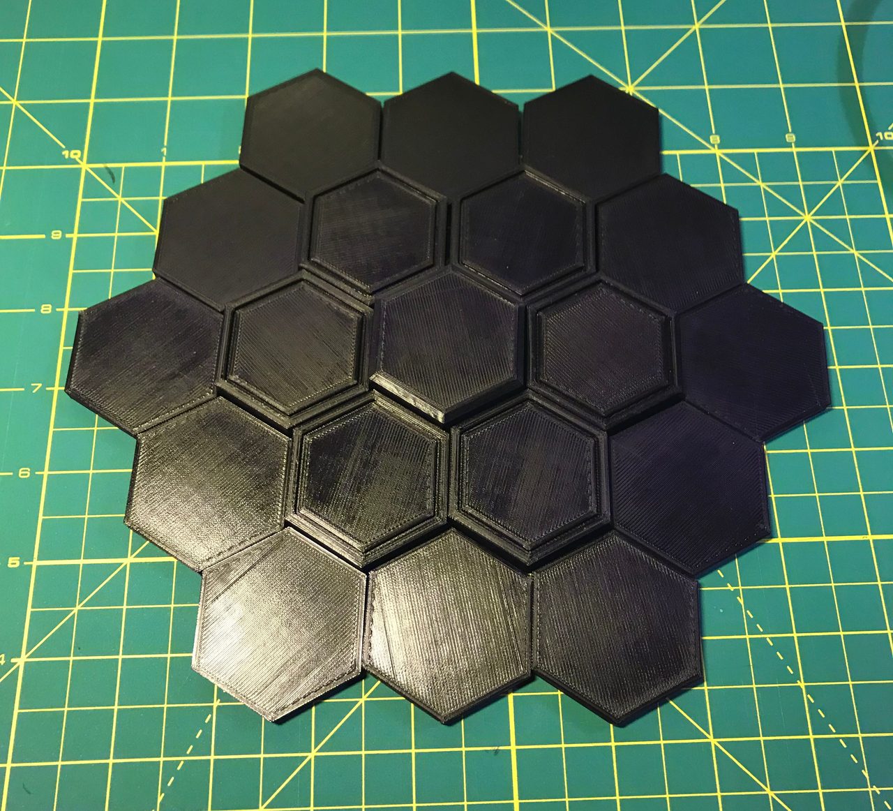 Unlabelled black 3D-printed hexagonal board sections fitted together on a green cutting mat.
