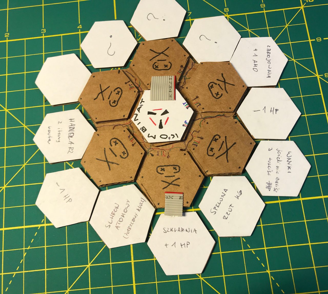 Early cardboard and paper hex-tile prototype with handwritten locations and improvised player markers.